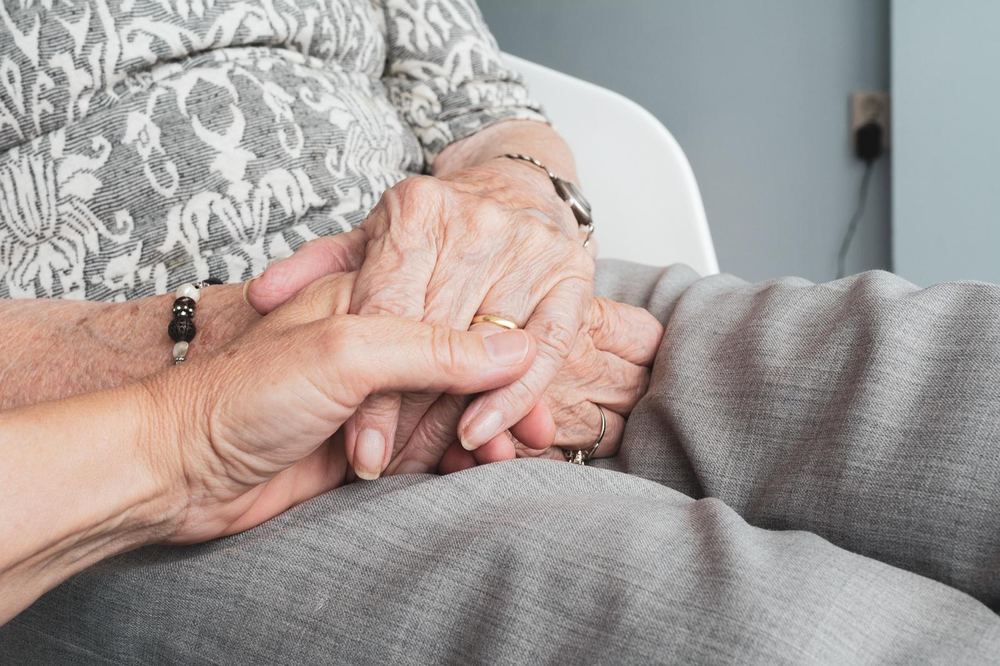 Les mans d'una cuidadora sostenint les d'una dona gran asseguda en una butaca
