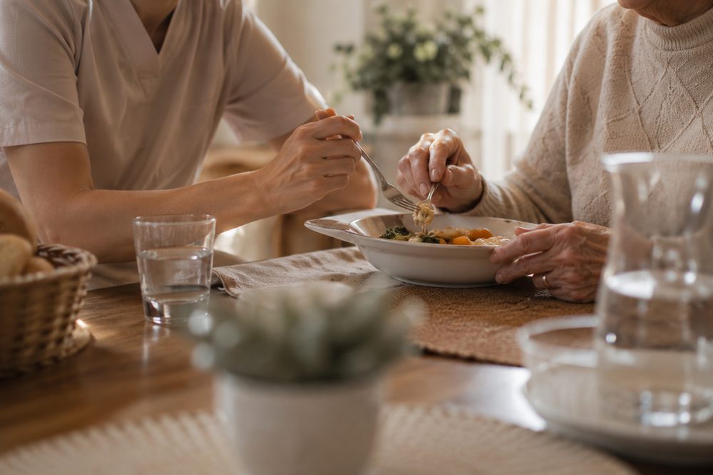 Una cuidadora acompanya una dona gran mentre dina a taula